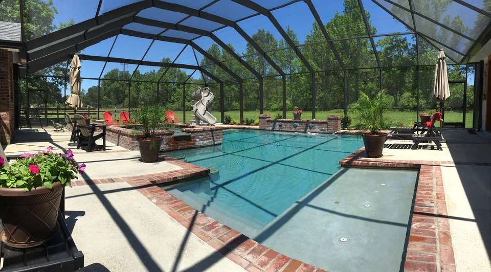 Screen enclosure surrounding a curved swimming pool and landscaped patio