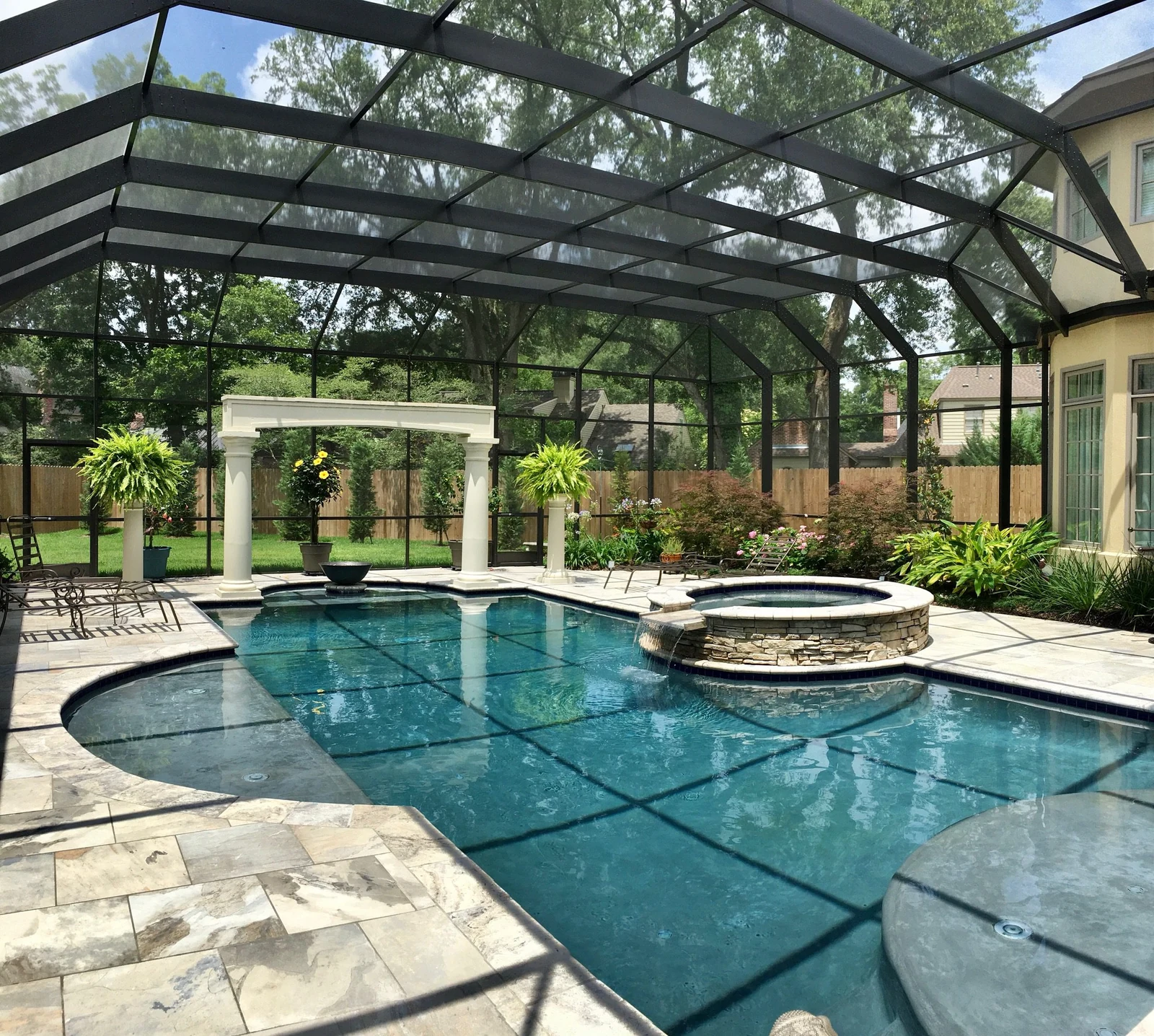 Custom pool enclosure framing a curved pool, spa, and garden beside a home